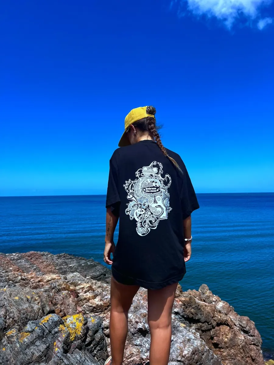 The same oversized black tee photographed from further back on the rocks